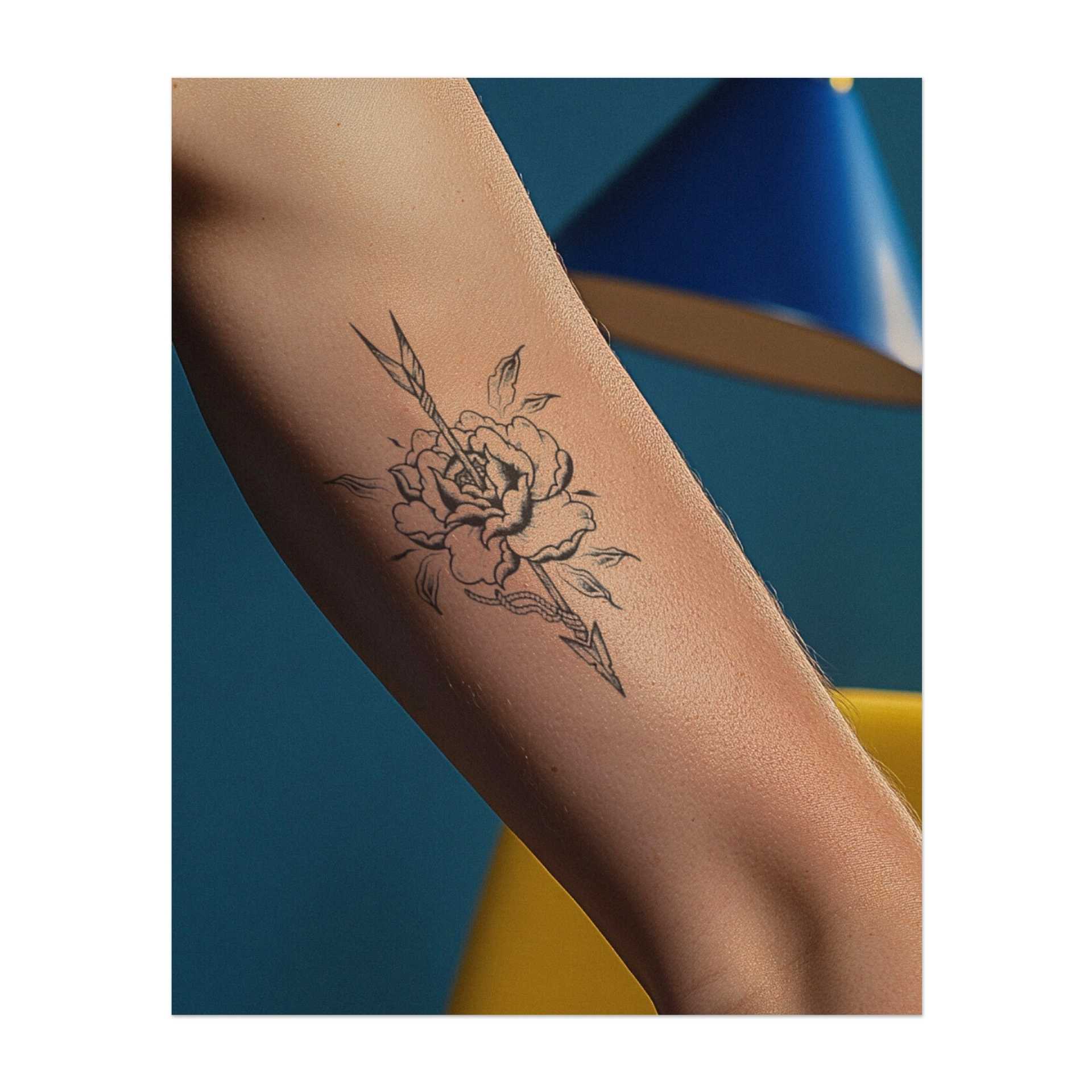 Eine wunderschöne Rose, durchbohrt von einem scharfen Pfeil, mit Blütenblättern und Blättern, die sich darum winden. Dieses Tattoo ist in einem zarten Stil gehalten und gibt ihm eine weiche, fast vintage Ausstrahlung. Es ist eine Mischung aus Eleganz und Stärke, perfekt für diejenigen, die Natur und Mut lieben.