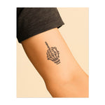 Une main squelettique faisant un geste rebelle symbolise le défi et l'individualité. Ce tatouage représente le fait de vivre sans excuses, d'accepter sa vérité et de faire preuve de force face à l'adversité.